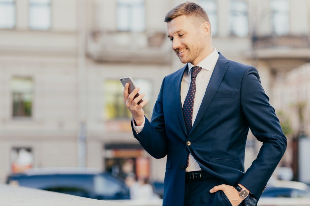 Businessman keeps hand in pocket, wears formal suit and wristwatch, receives notification