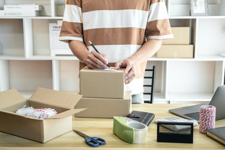 Male entrepreneur is writing address on cardboard boxes for prep